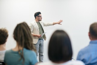 Person präsentiert vor einer Gruppe von Zuhörern Person präsentiert vor einer Gruppe von Zuhörern