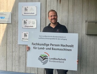Person hält ein Schild mit der mit der Aufschrift Fachkundige Person Hochvolt für Land- und Baumaschinen