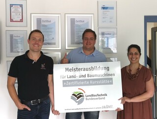 Drei Personen posieren vor einem Schild mit der Aufschrift Meisterausbildung für Land- und Baumaschinen